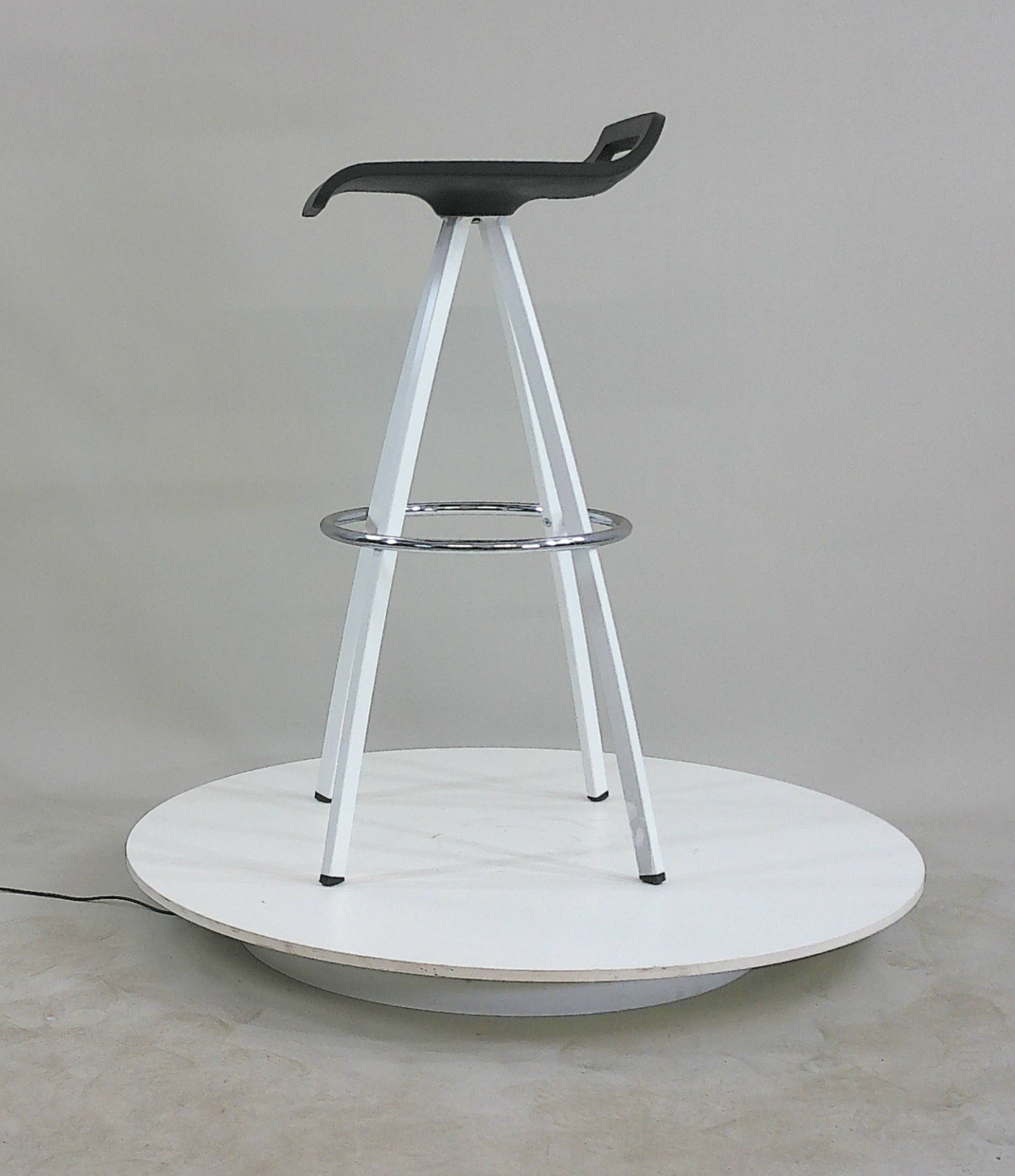 Bar stool sitting on a grey back ground with white powder coated 4 leg base and black seat with low back and photographed side on